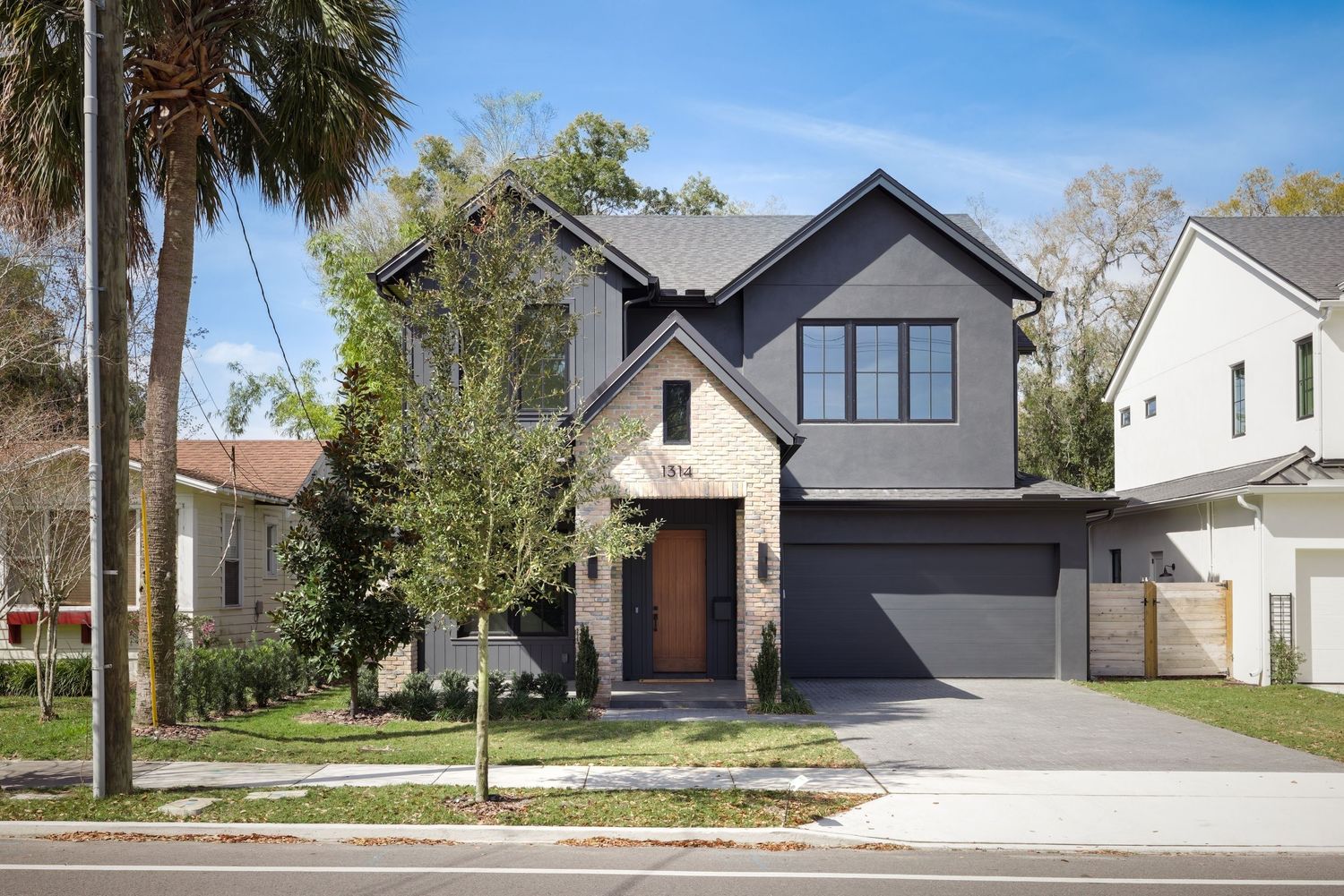 Contemporary dark gray two-story home with stone accents, attached garage, and mature street trees.