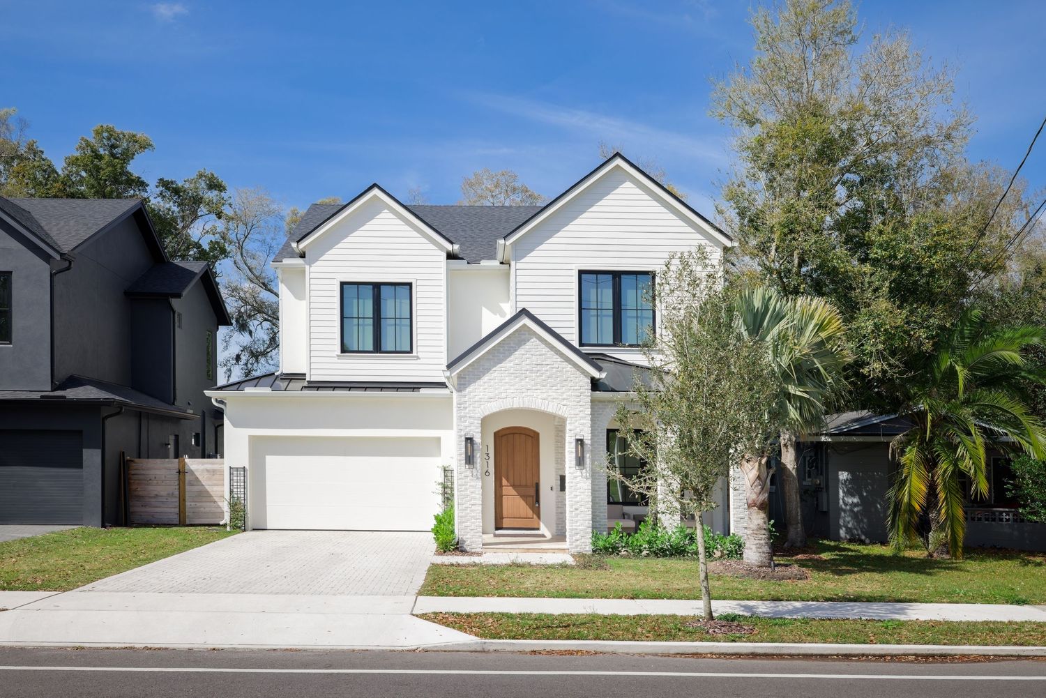 Modern two-story white farmhouse with black-trim windows, arched entry door, two-car garage, and manicured front lawn.