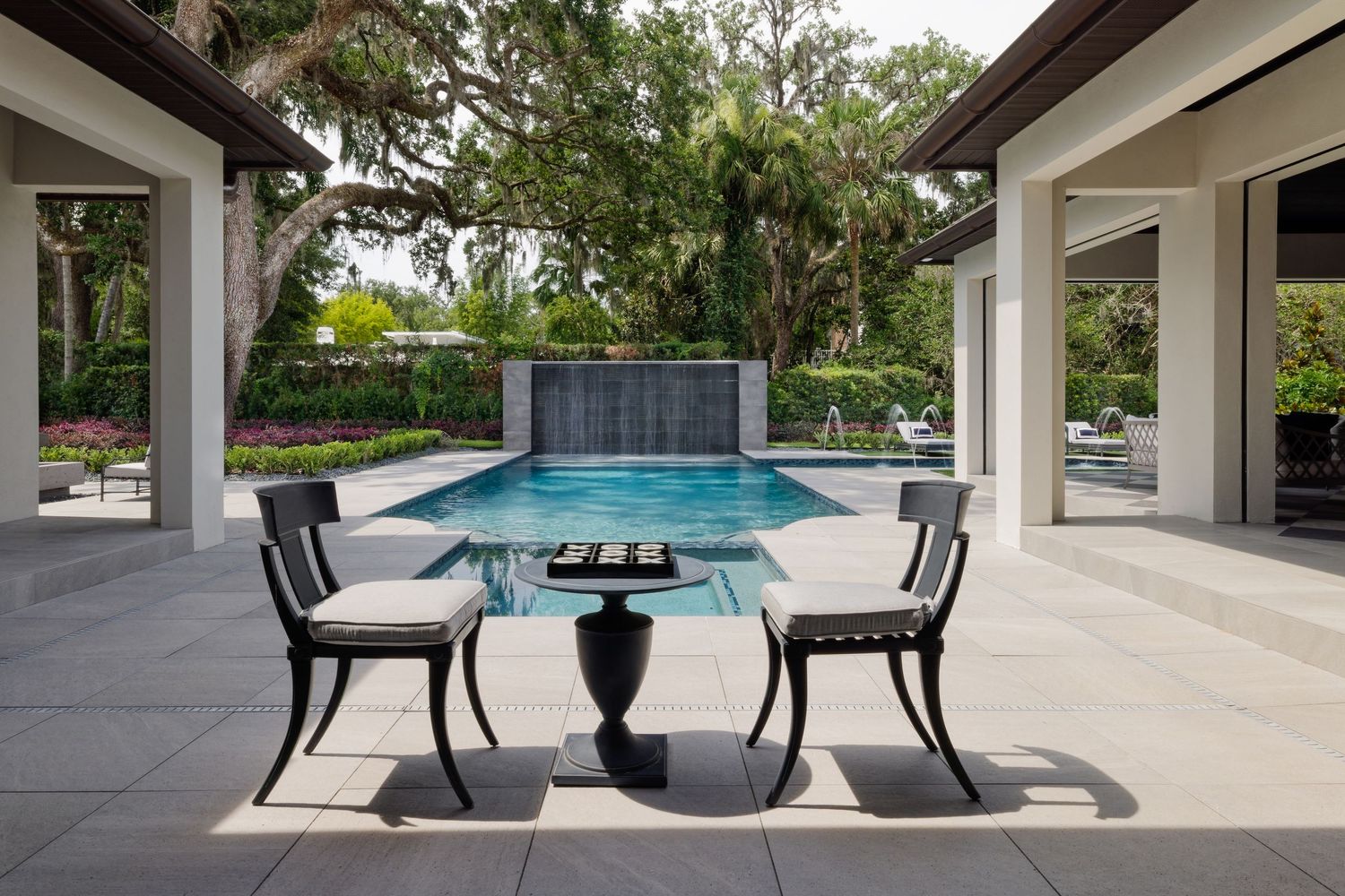 Upscale patio seating area with black bistro table and chairs overlooking a serene pool and lush garden.