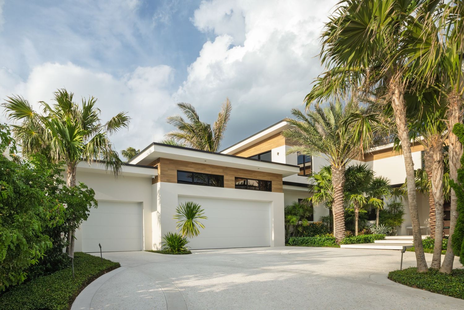 Modern white stucco home exterior with triple garage, tropical palm trees, and curved driveway in Florida.