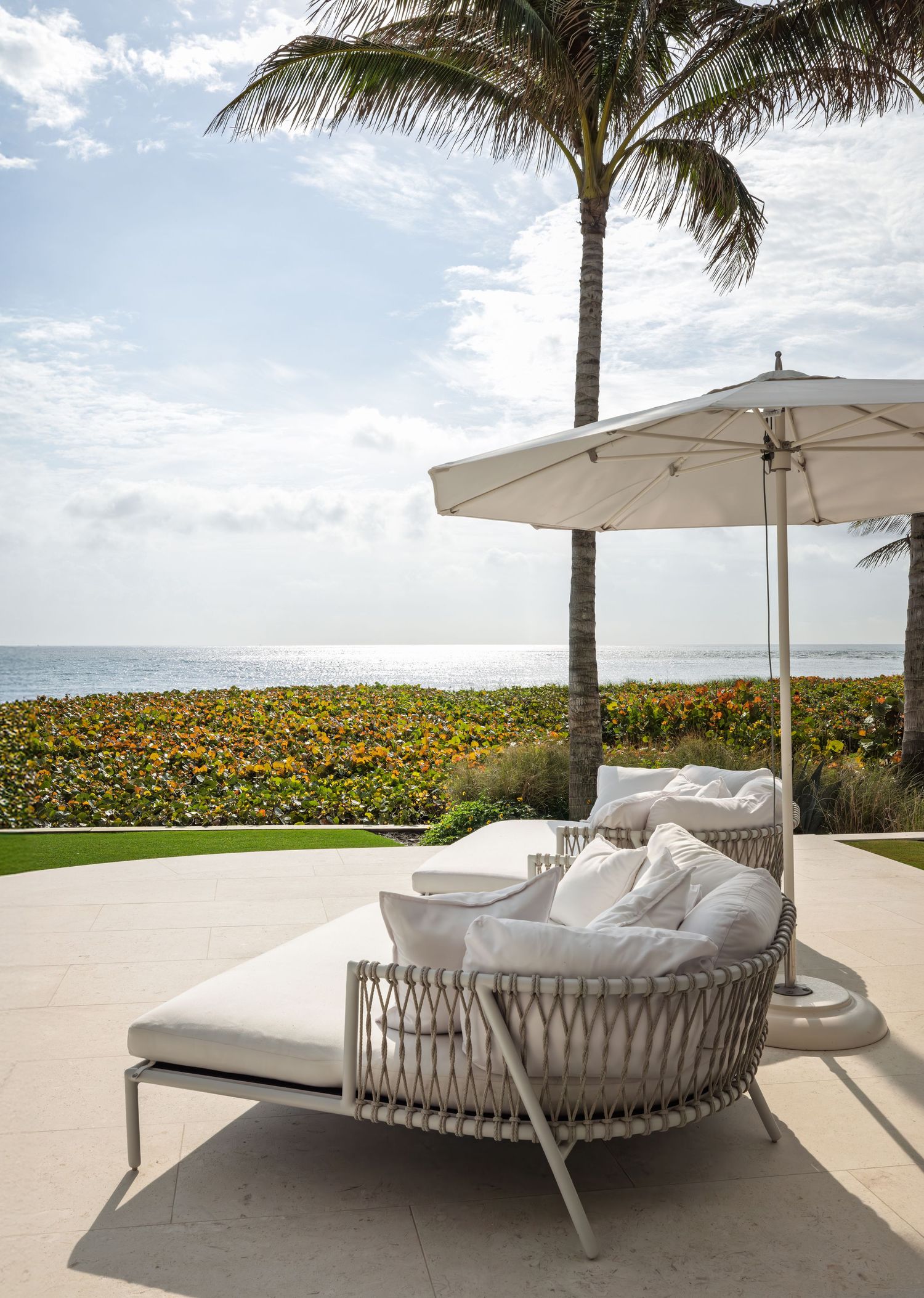 Luxurious outdoor patio with white lounge chair, umbrella, palm tree, and ocean view.