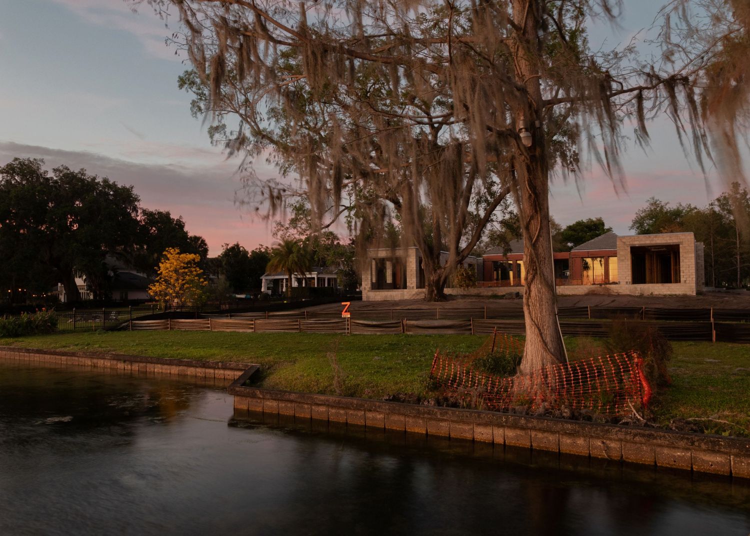 Dusk view of waterfront property with Spanish moss trees, canal reflection, and warm glowing home lights.