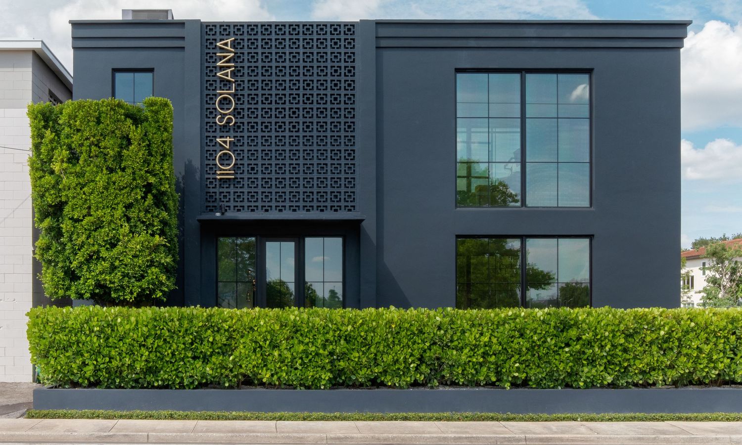 Modern dark gray two-story commercial building with decorative lattice panel and manicured green hedges.