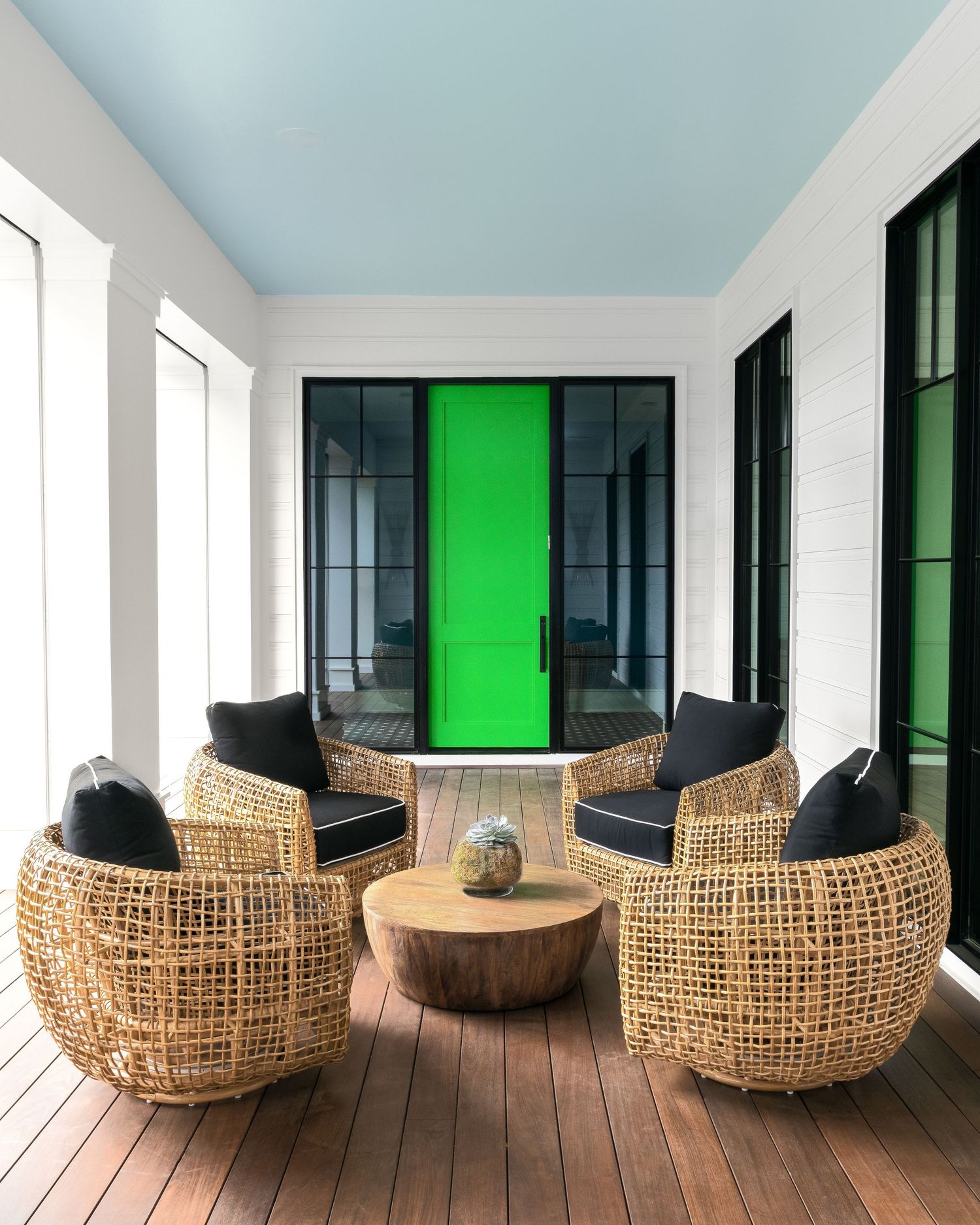 Covered porch with wicker barrel chairs, wood ceiling painted blue, and a bold green front door.