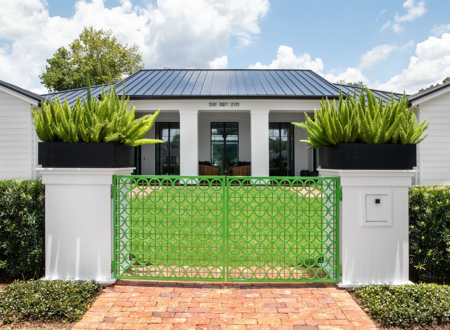 White cottage exterior with bright green ornate gate, tall snake plant planters, and black metal roof.