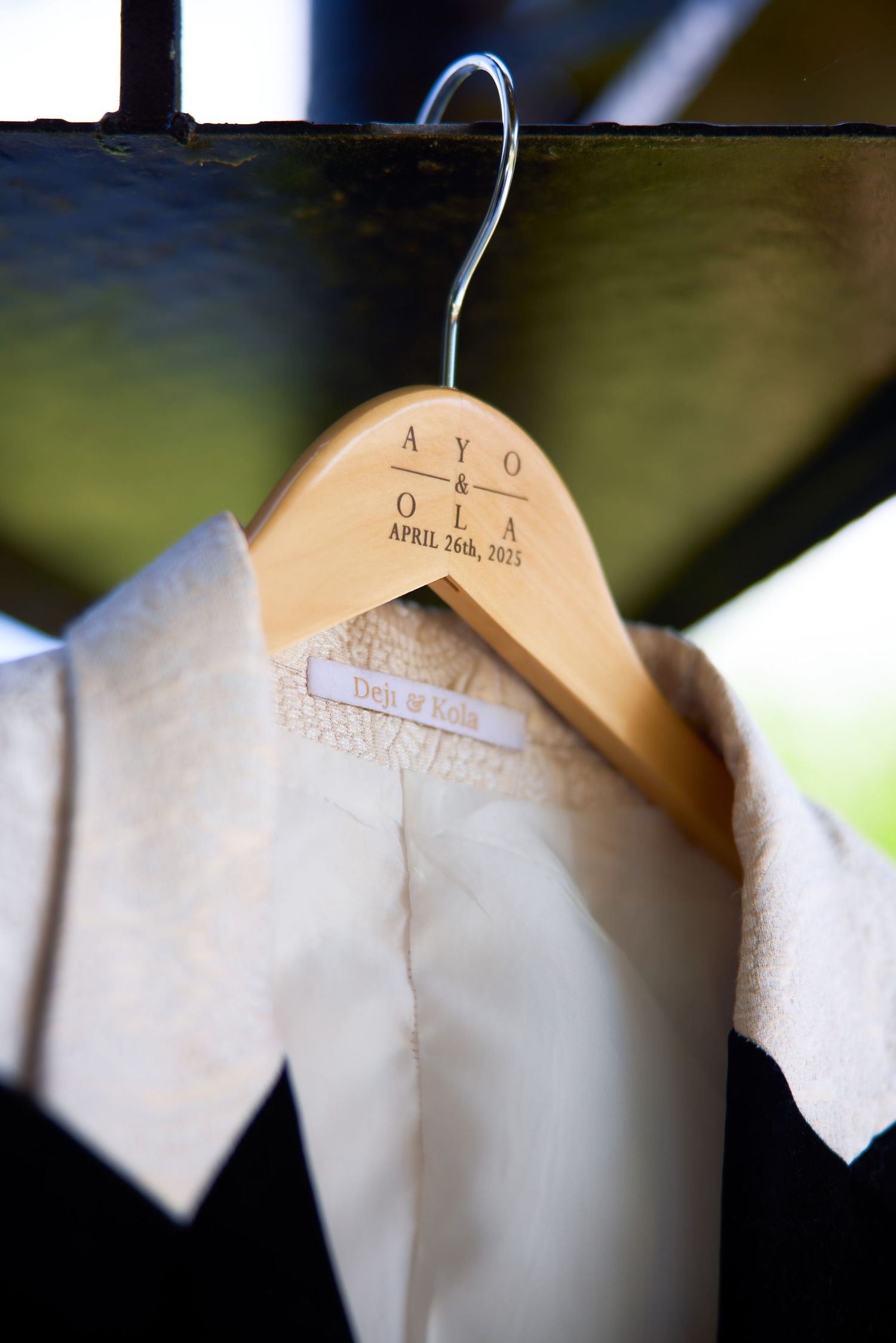 Custom wooden wedding hanger engraved with Ayo & Ola April 26th, 2025, holding a white wedding garment.