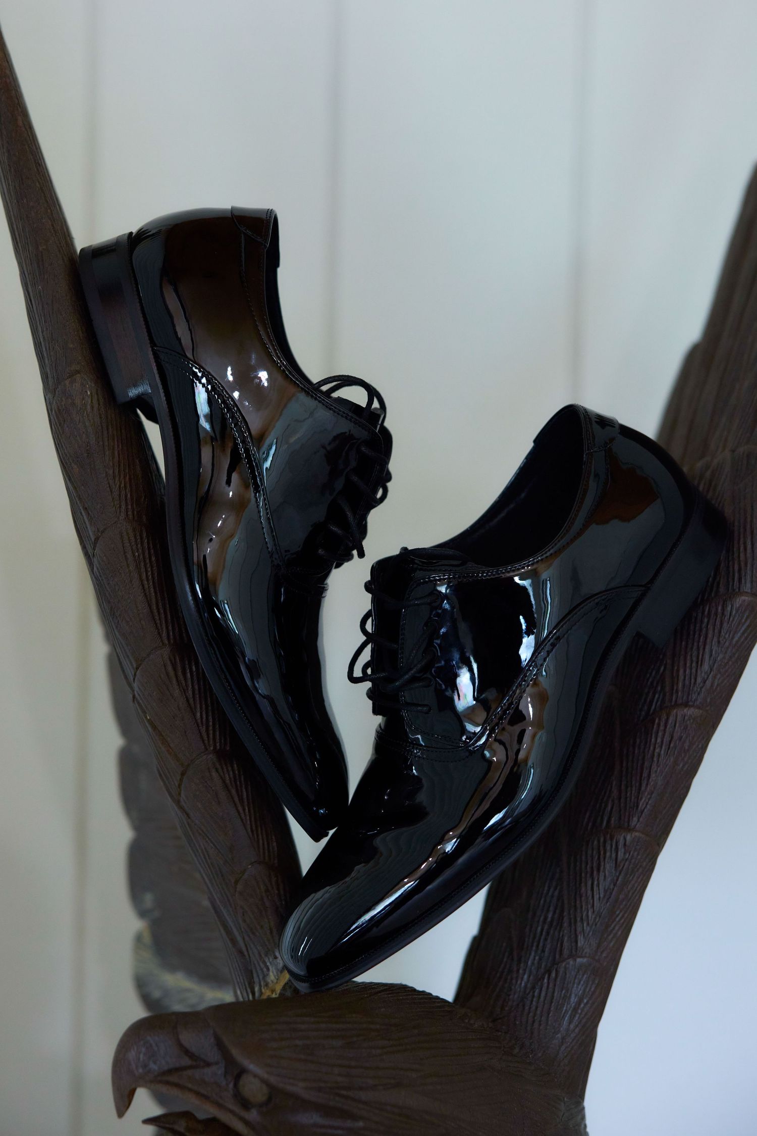 Shiny black patent leather lace-up oxford dress shoes displayed on a wooden eagle sculpture.