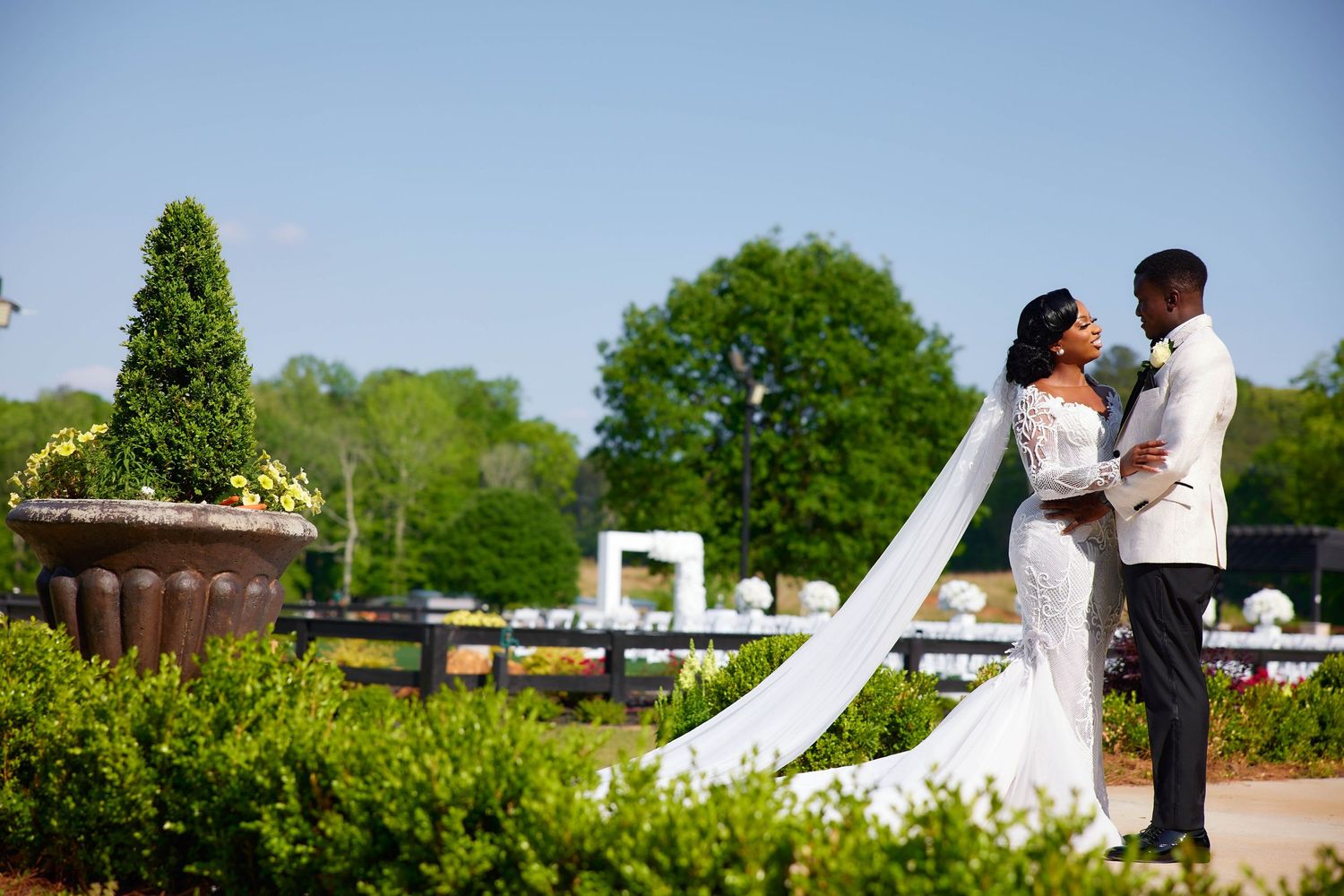Elegant bride and groom pose in lush garden setting, bride's veil flowing, on their wedding day.