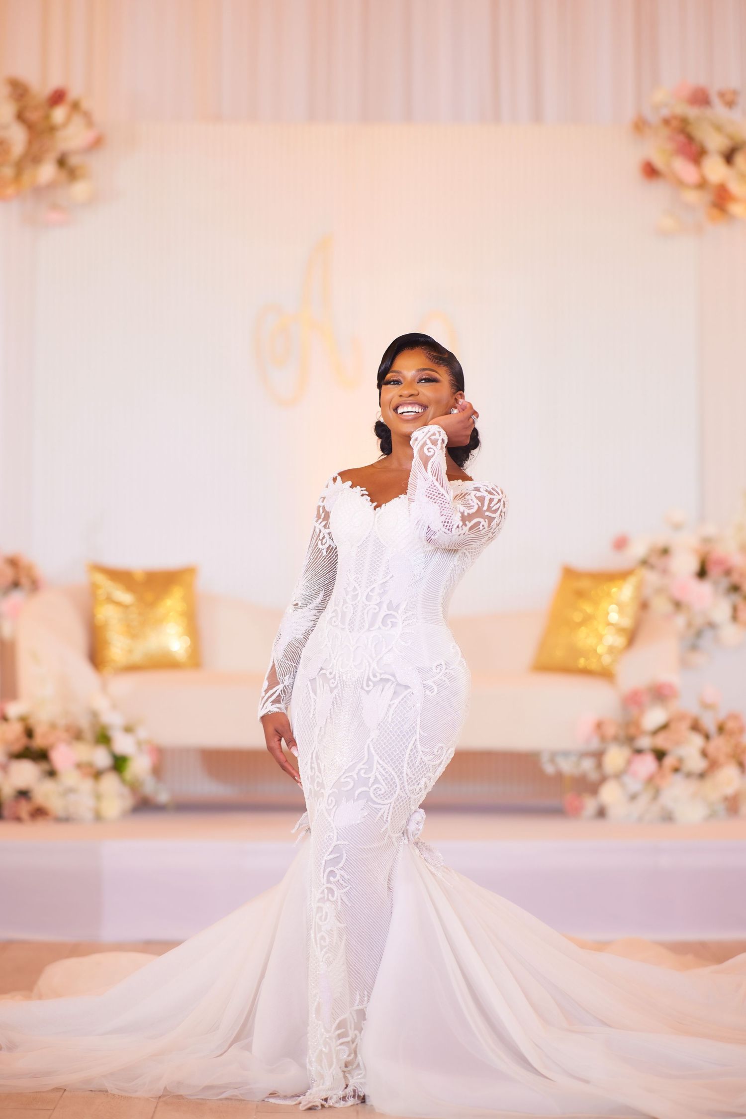 A bride in a white lace mermaid gown with long sleeves poses elegantly at a floral wedding reception venue.