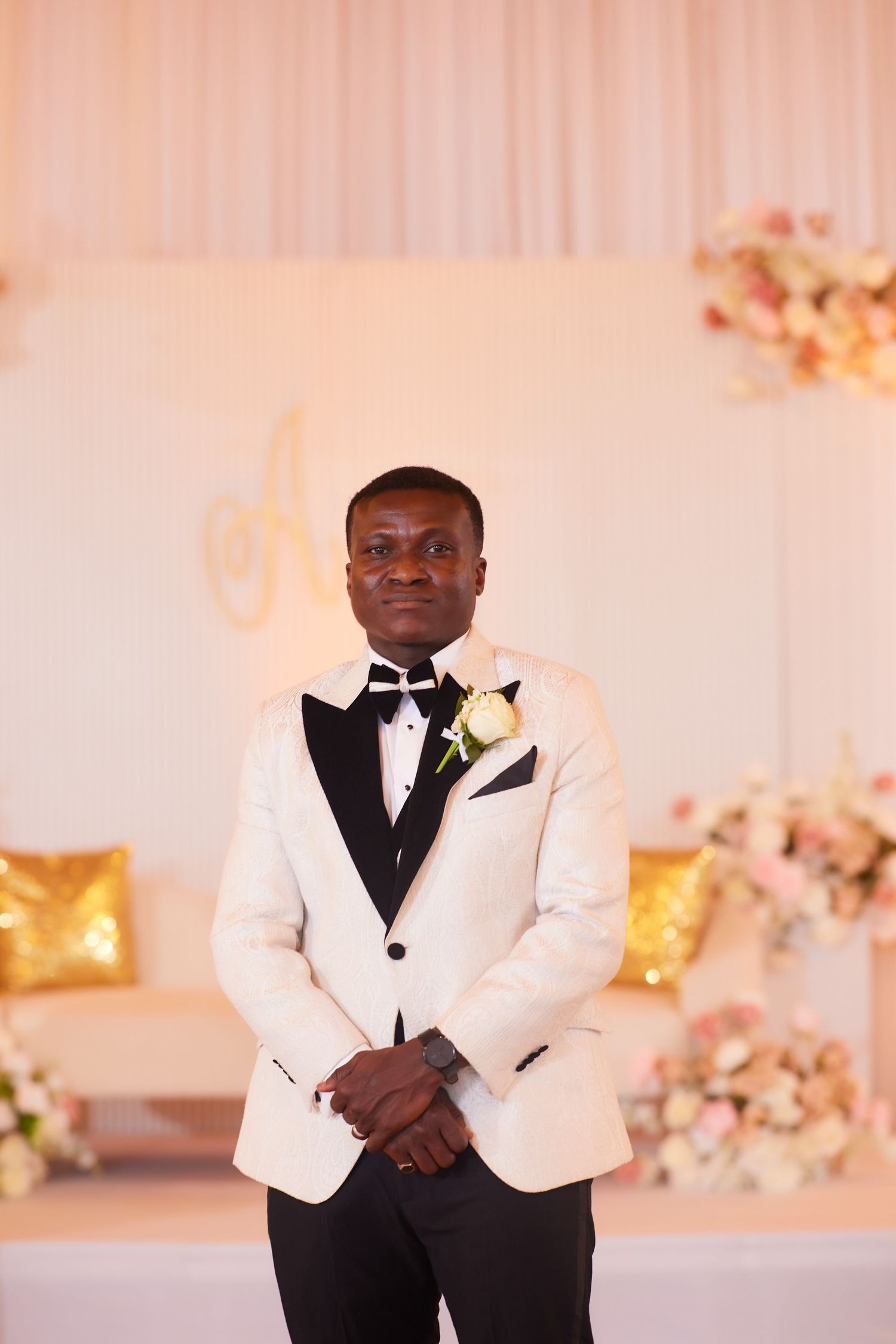 Handsome groom in white tuxedo with boutonniere standing at decorated wedding reception.