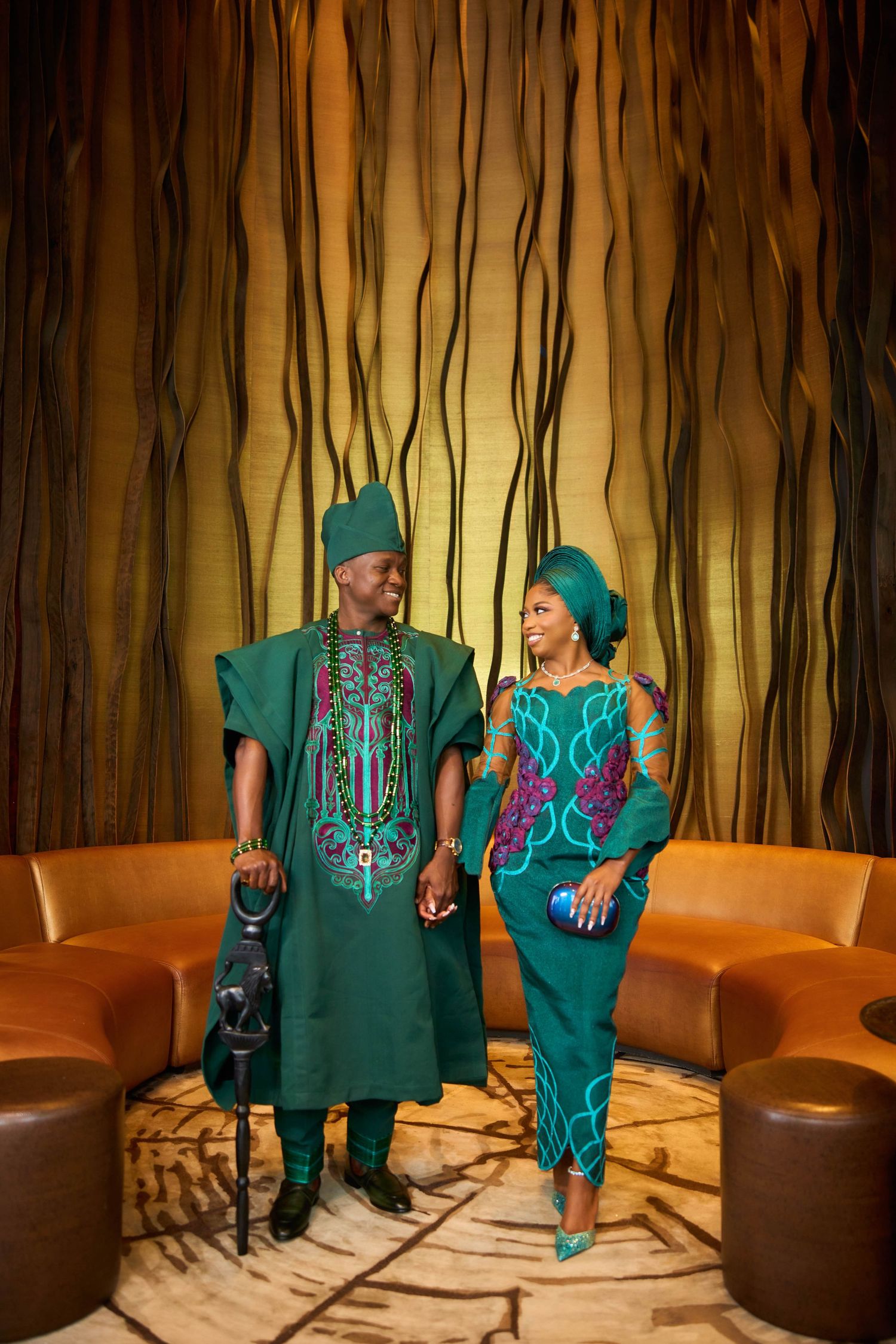 Couple smiling in coordinating green traditional Nigerian Yoruba outfits, holding hands indoors.