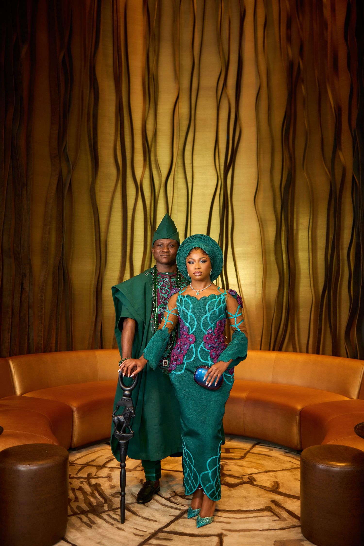 Couple in matching emerald green traditional Nigerian Yoruba attire with embroidery, posing indoors.
