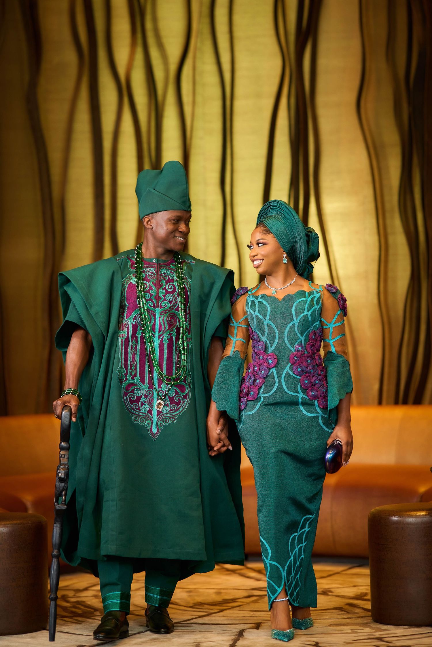 Couple in matching emerald green traditional Nigerian Yoruba attire with purple embroidery, holding hands at a formal event.