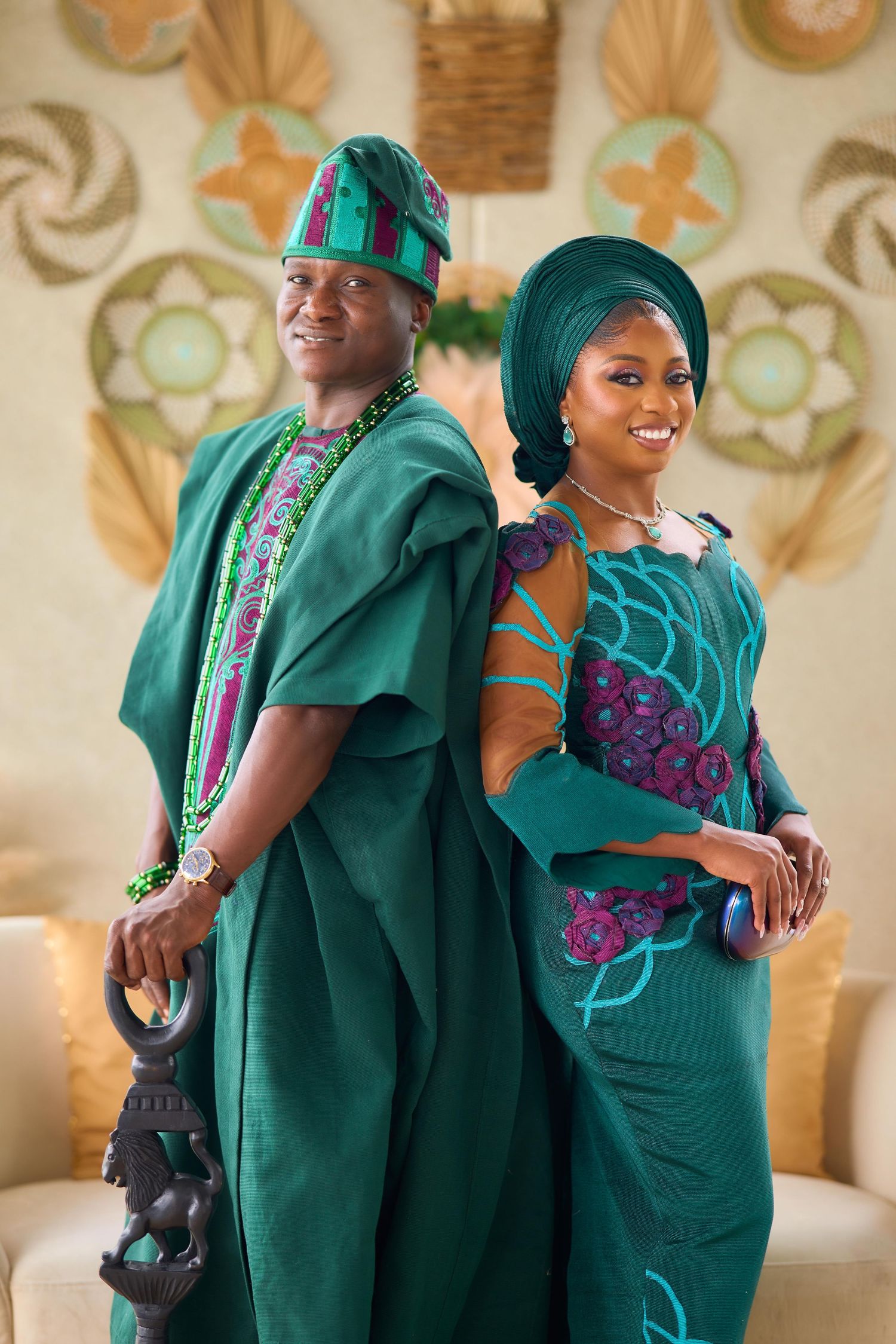 Nigerian couple in matching teal traditional Yoruba attire, agbada and gele, posing back-to-back at a cultural ceremony.