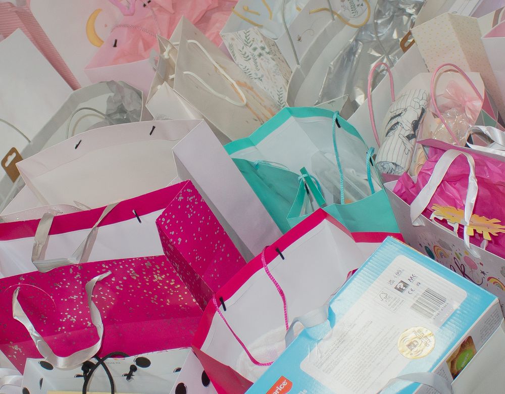 Colorful gift bags and presents piled together featuring pink, teal, and white designs for a celebration.