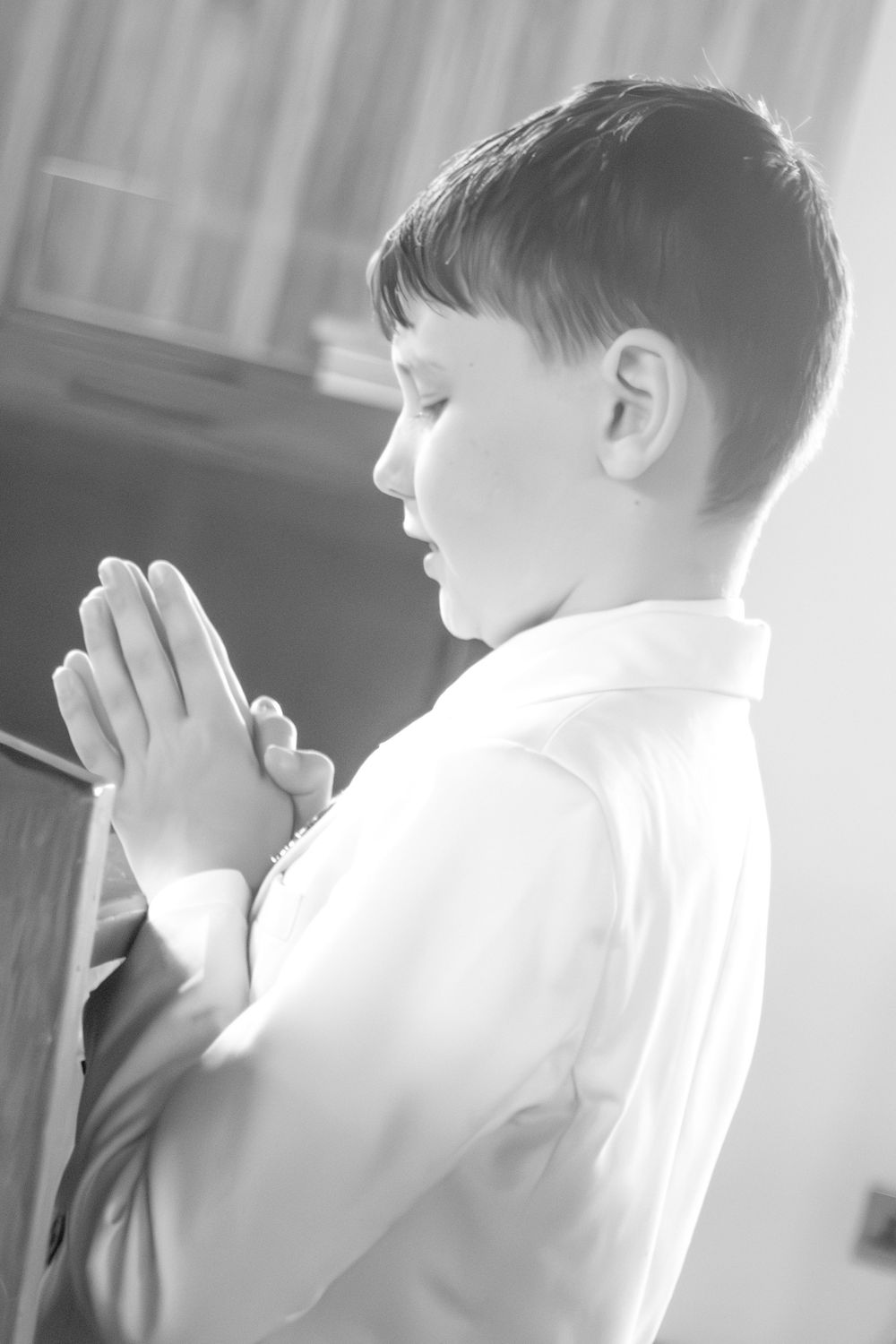 Black and white photo of a boy praying with hands clasped at a church pew.