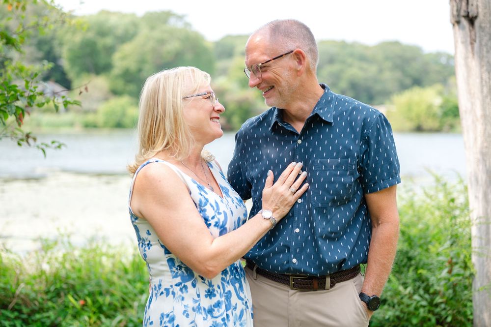 Happy couple laughing together outdoors by a lake, woman in floral dress and man in navy shirt.