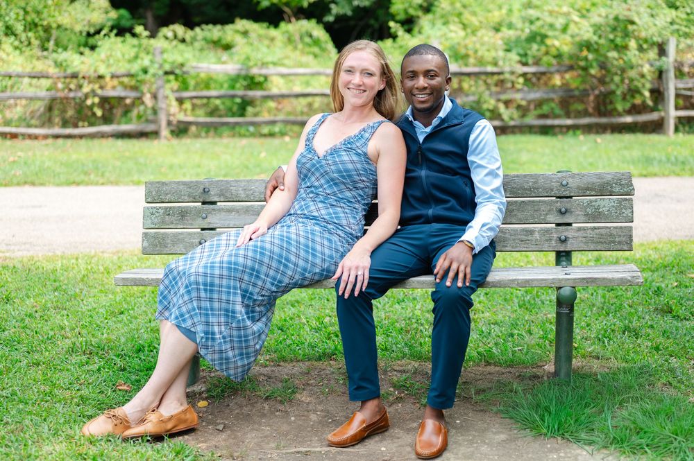Smiling couple sitting together on a wooden park bench outdoors on a sunny day.