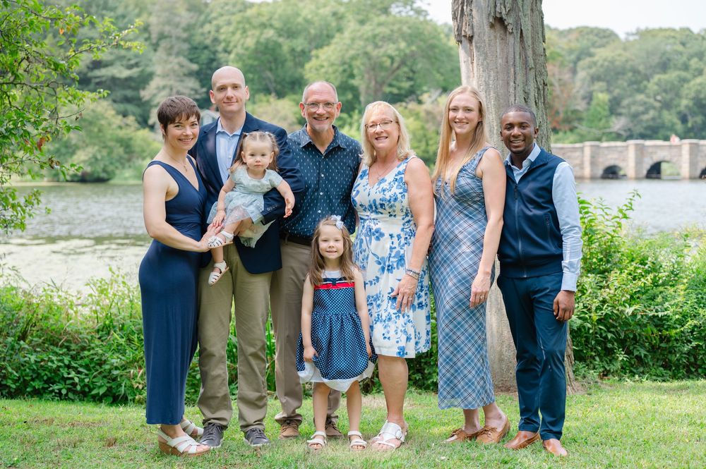 Extended family group portrait outdoors near a river with green trees in background.