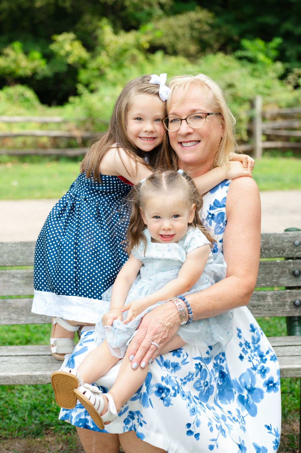 Grandmother sitting on bench with two young granddaughters in matching blue floral outfits.