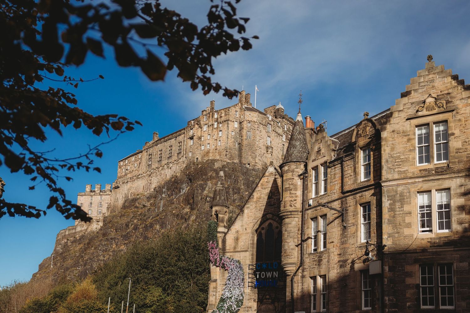 Edinburgh Castle perched atop volcanic rock overlooking historic stone buildings under a bright blue sky.
