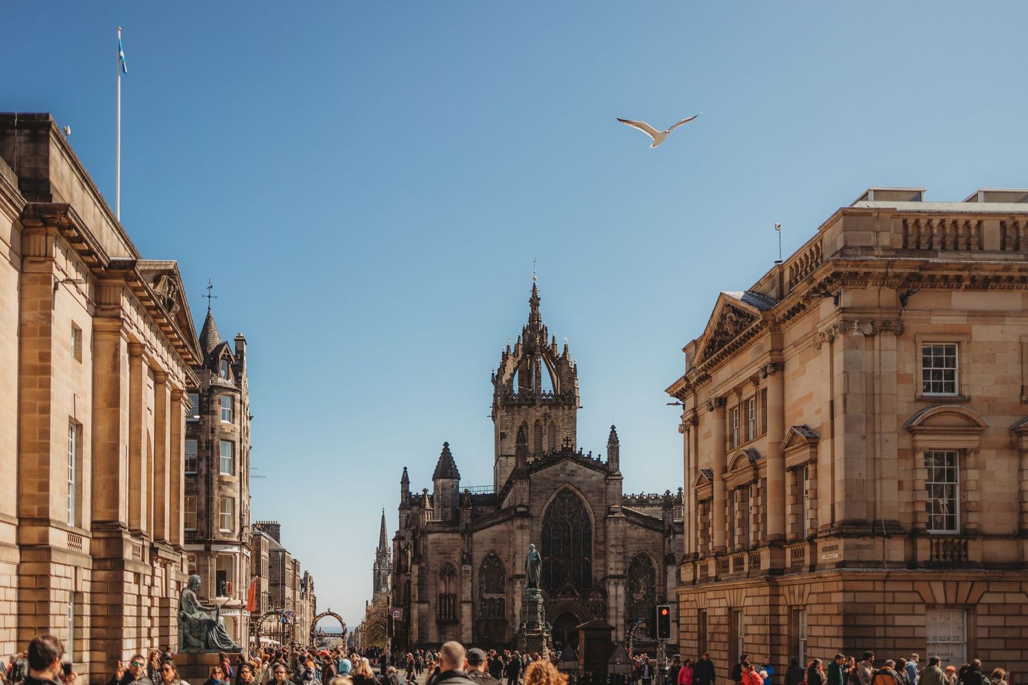 Busy Royal Mile street in Edinburgh with St Giles Cathedral and historic buildings under a clear blue sky.