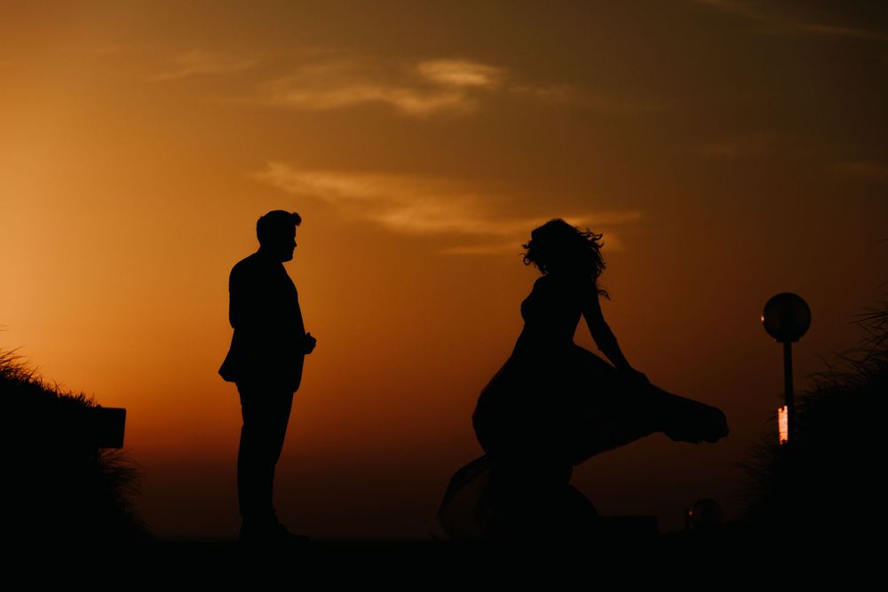 Couple silhouetted at sunset, bride twirling her dress in the warm evening light.