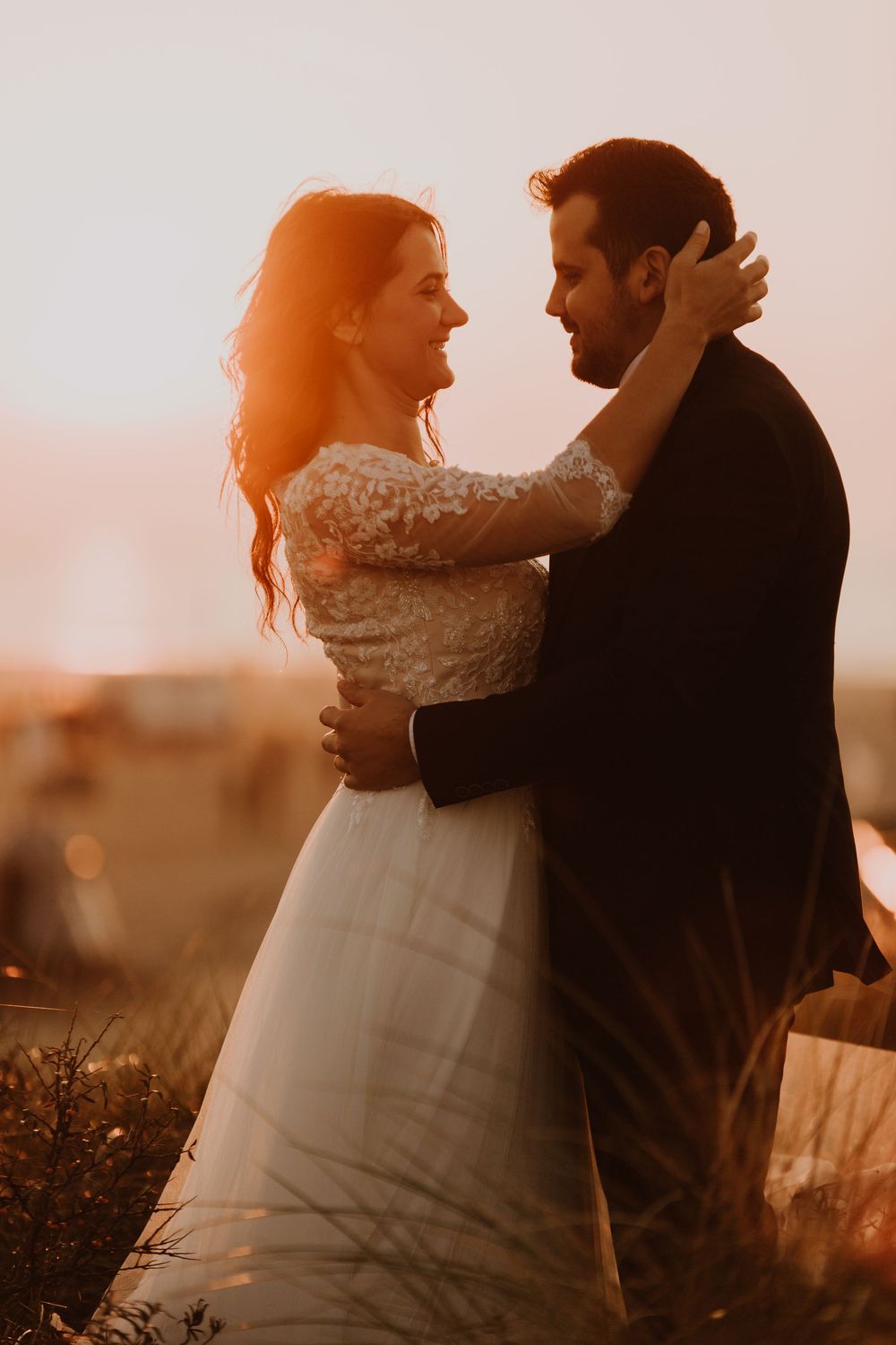 Bride and groom gazing at each other lovingly while embracing in sunset light.