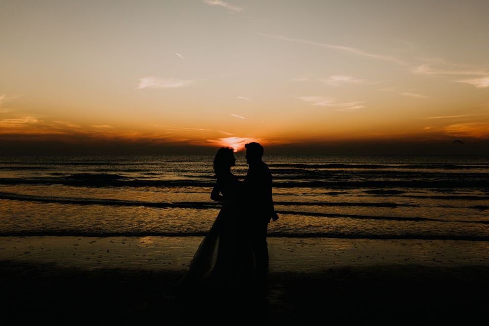 Silhouette of bride and groom facing each other on beach with stunning golden sunset backdrop.