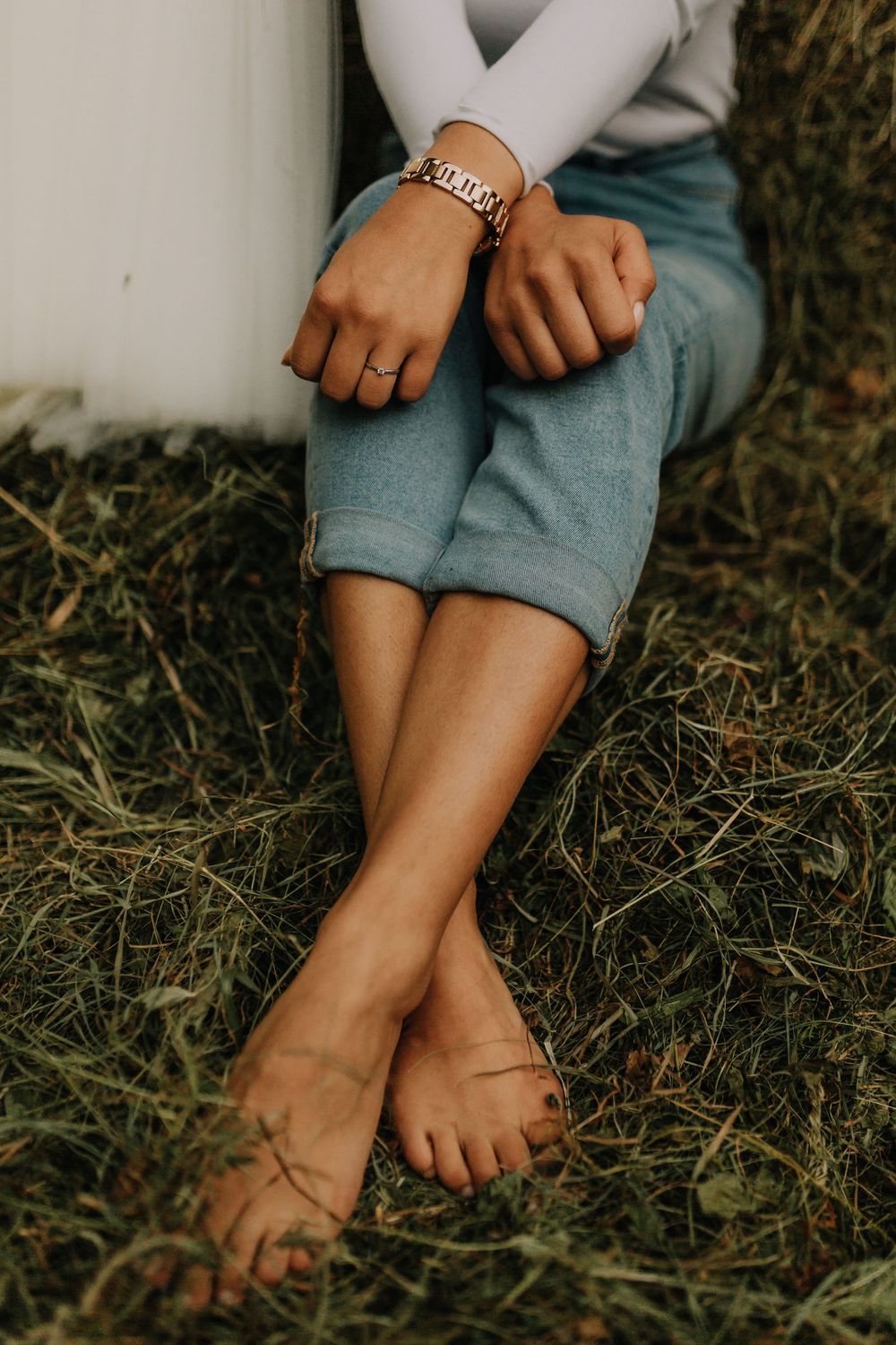 Close-up of brides bare feet and hands wearing bracelet and ring while sitting on green grass.
