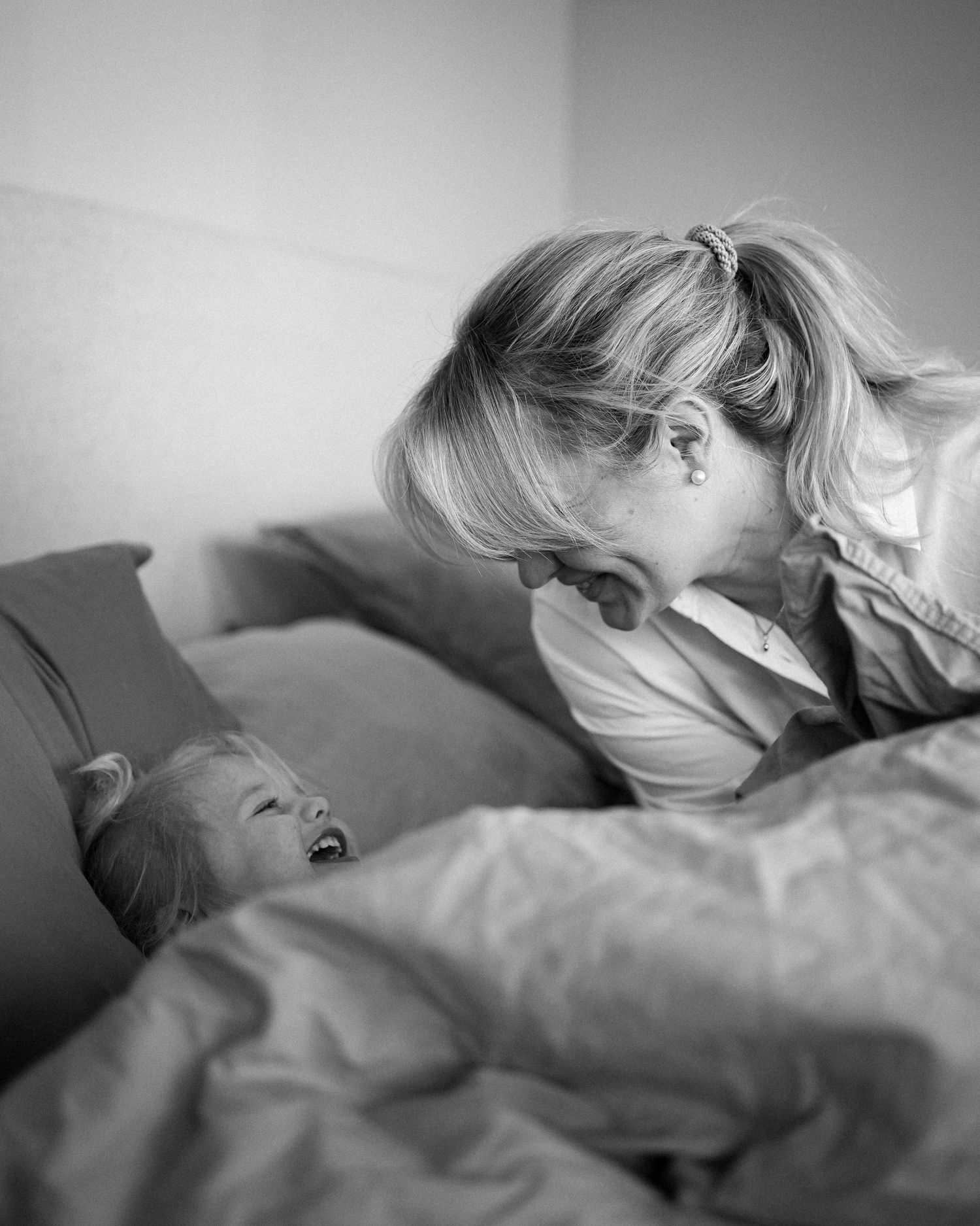 En mamma och hennes lilla dotter busar i sängen. De tittar på varandra och skrattar.