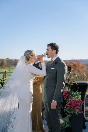 Bride and groom sharing a drink during outdoor fall wedding ceremony with scenic countryside views.