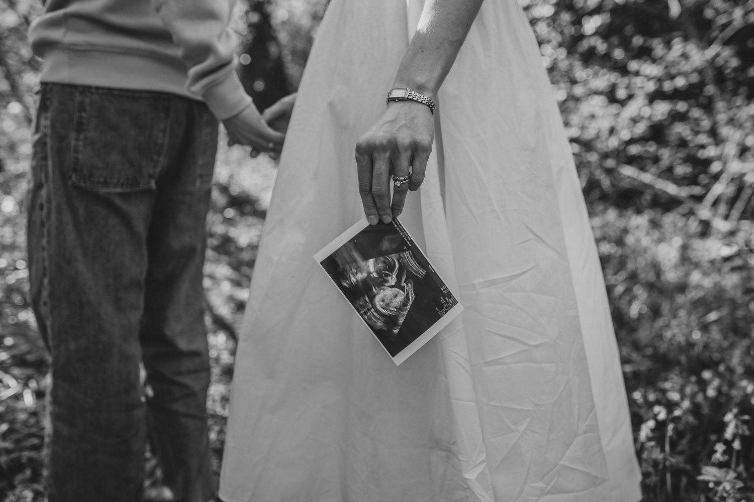 Couple holding hands and ultrasound photo in black and white maternity announcement outdoor portrait.
