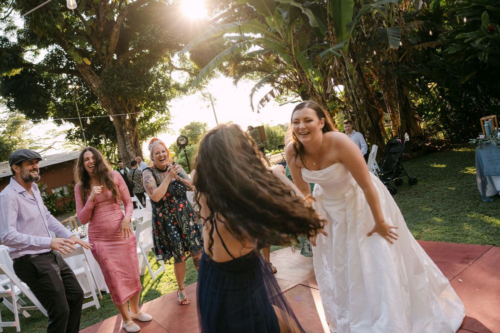 Bride in white dress dancing joyfully with guests at outdoor garden wedding reception.