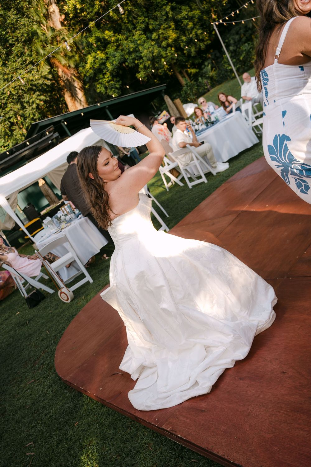 Bride in white wedding gown twirling on outdoor dance floor at garden reception.