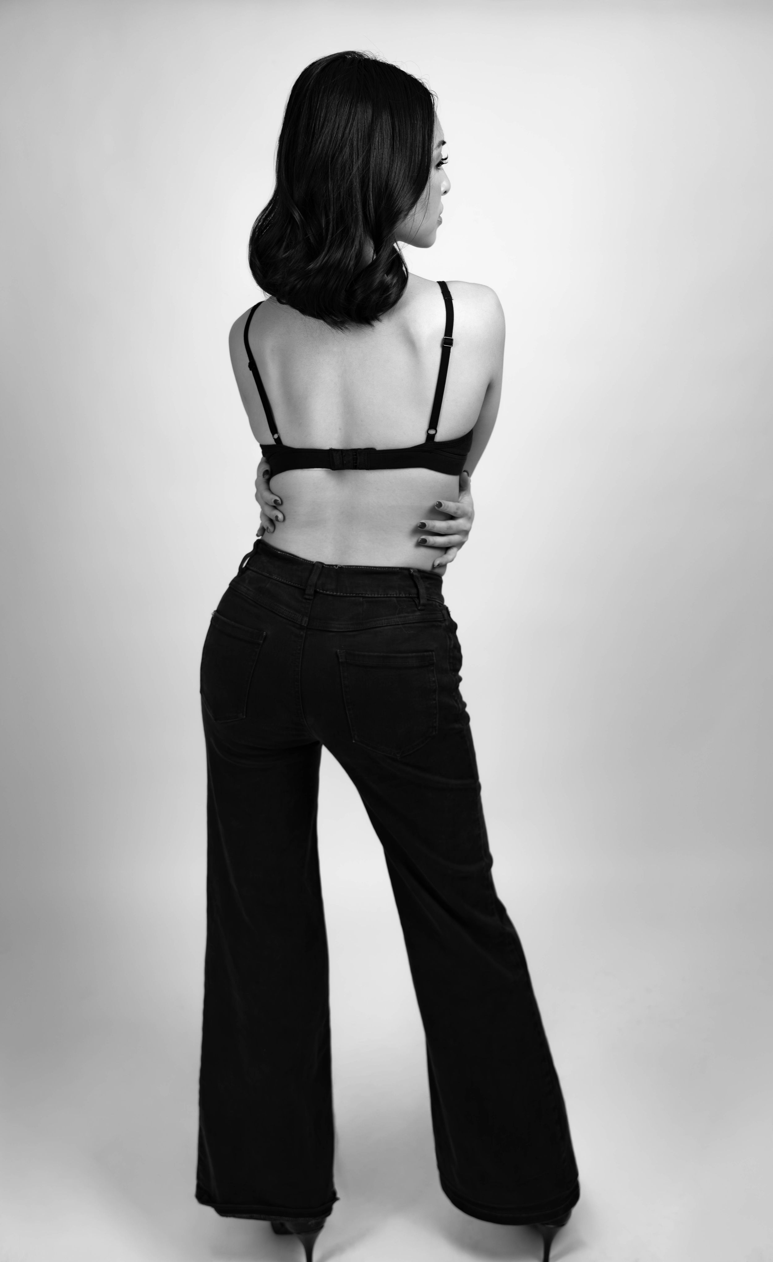 Black and white photo of a woman in wide-leg pants and a bralette, posing with her back to the camera.
