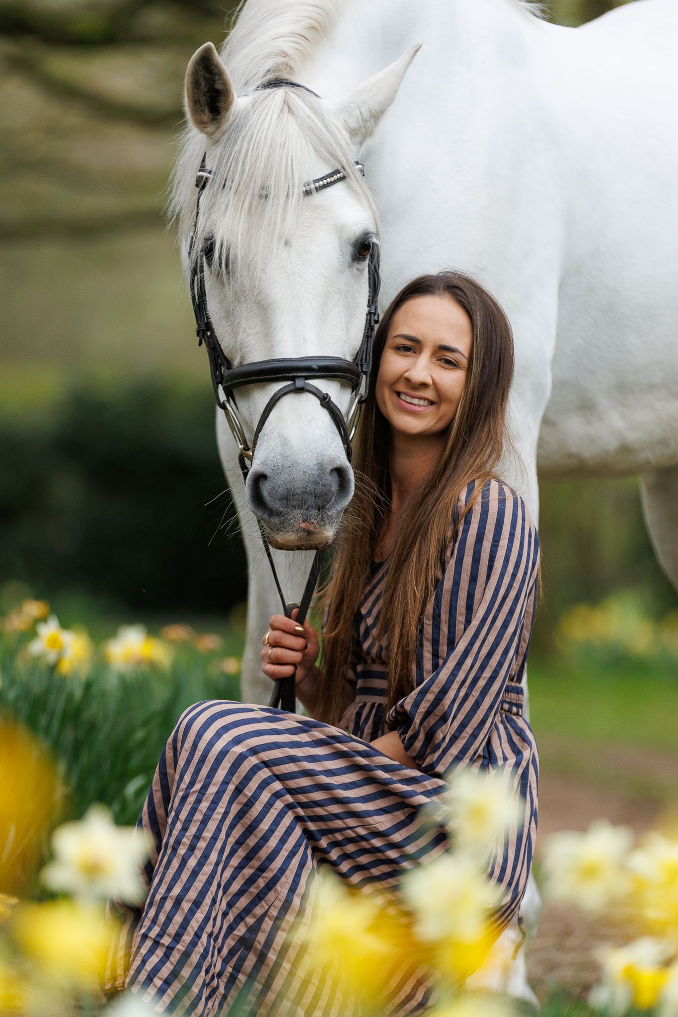 Young girl kneeling beside a horse in a black and white countryside photo near a stone building.
