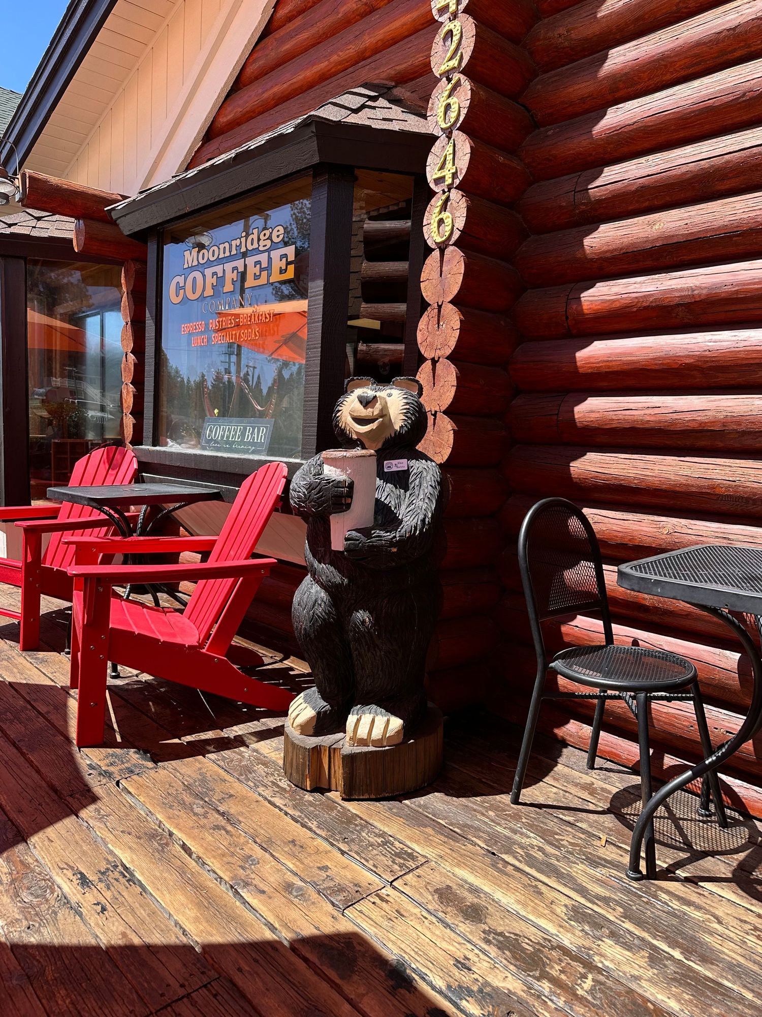 Moonridge Coffee log cabin exterior with carved wooden bear statue, red Adirondack chairs, and rustic deck seating area.