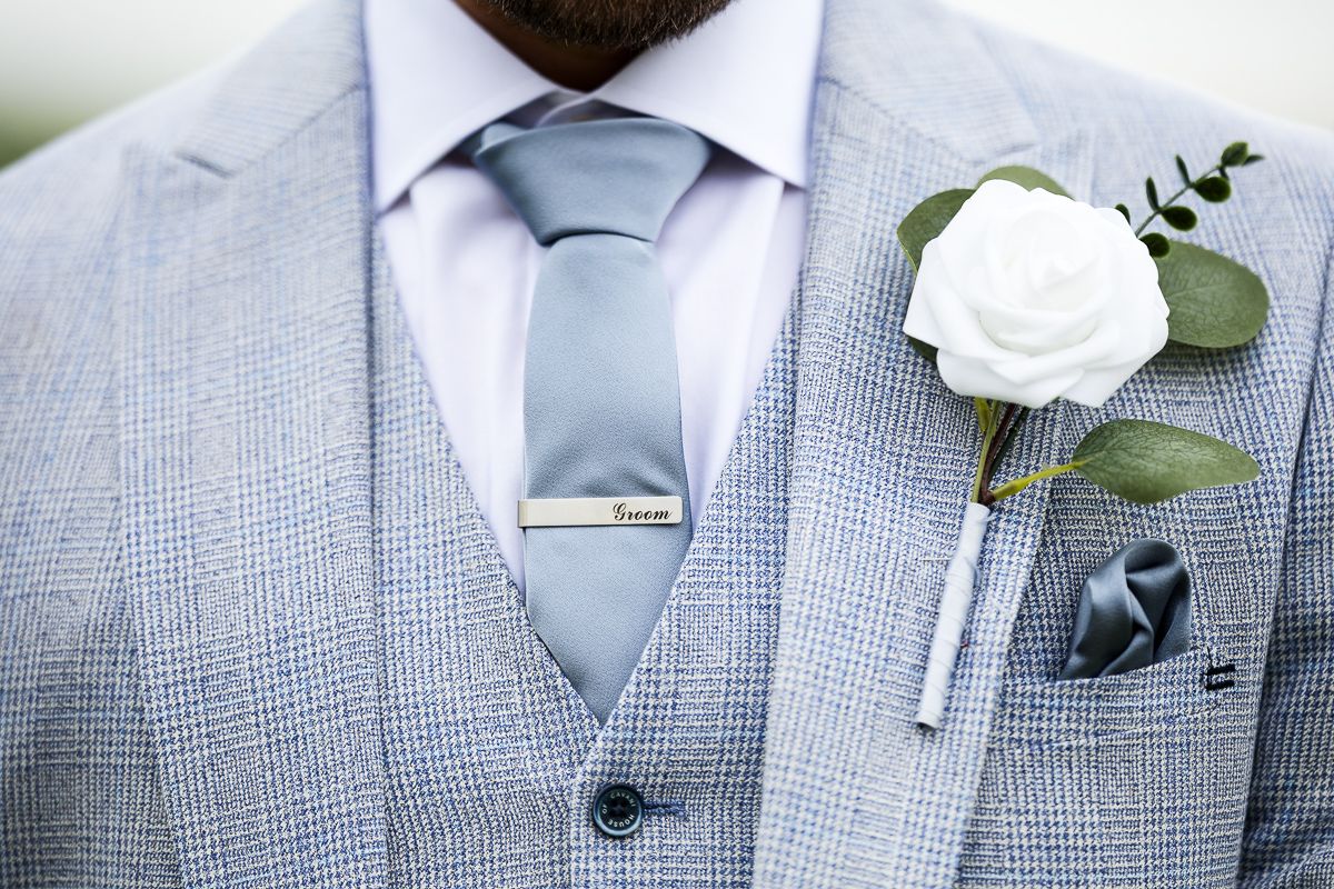 Groom wearing light blue suit vest and tie with white rose boutonniere and pocket square at wedding.