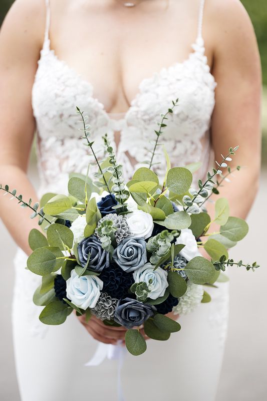 Bride holding a wedding bouquet with navy, dusty blue, and white roses accented by eucalyptus greenery.
