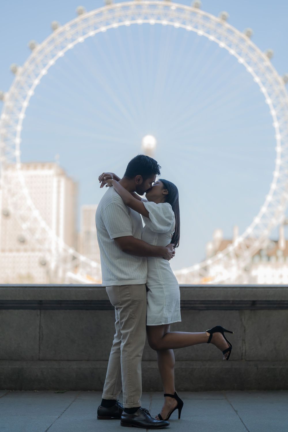 Couple sharing a romantic kiss in front of the London Eye Ferris wheel at dusk.