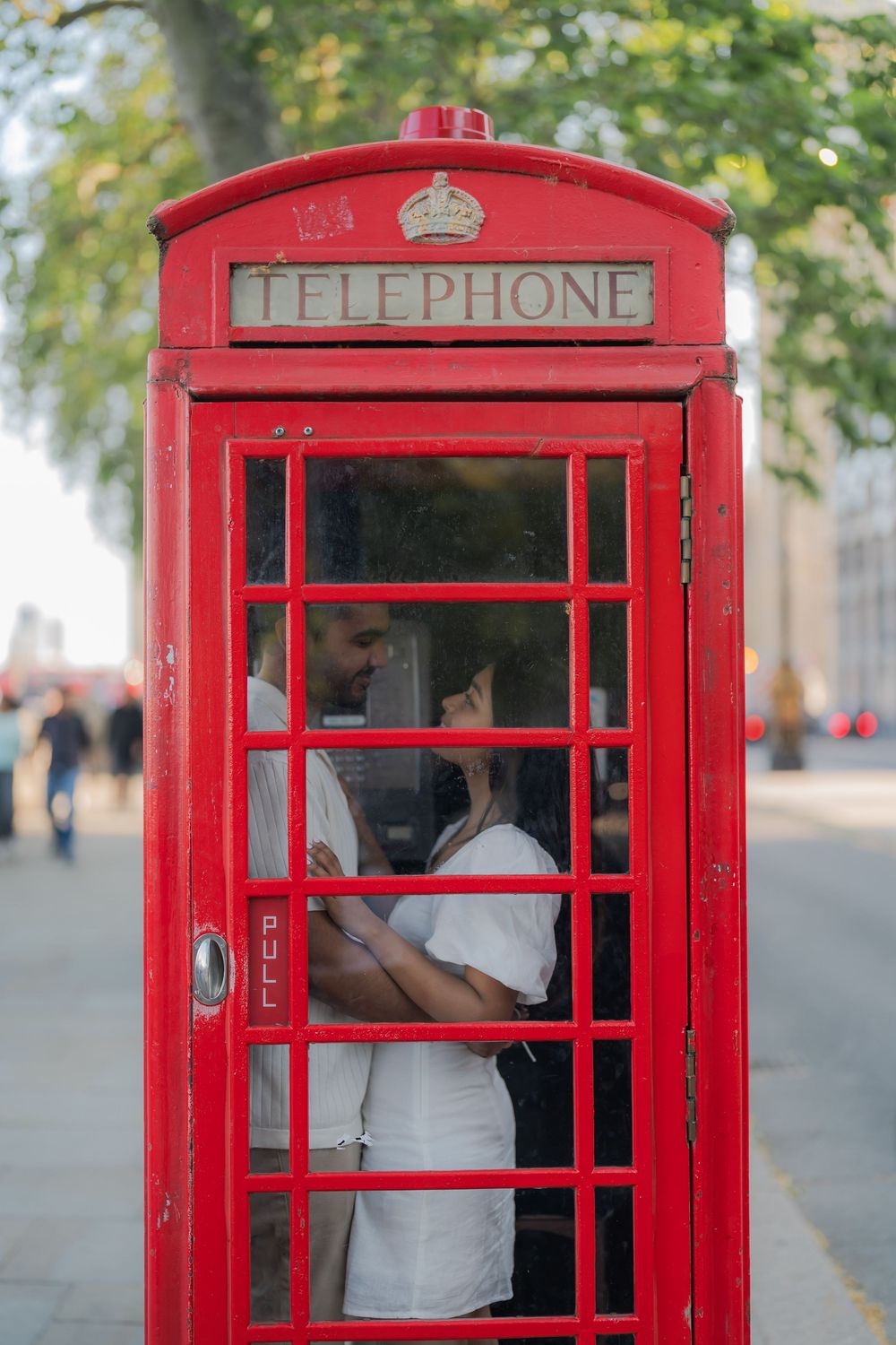 Couple sharing a romantic moment inside a iconic red British telephone box on a London street.