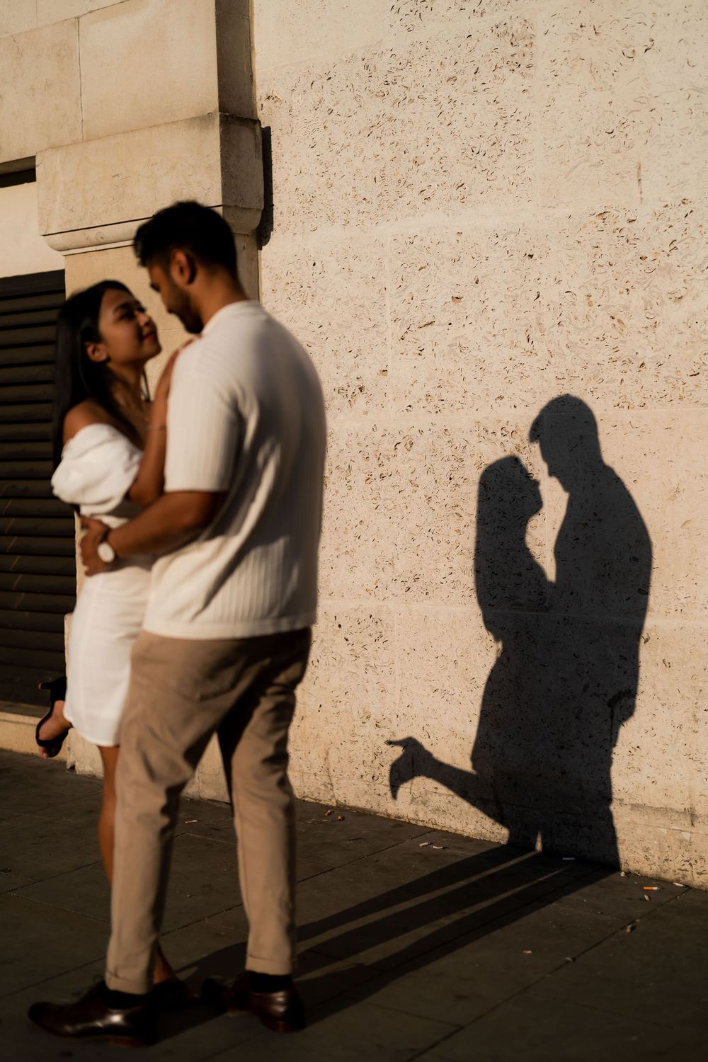 Romantic couple embracing near a sunlit wall with their silhouette shadow, captured during golden hour.