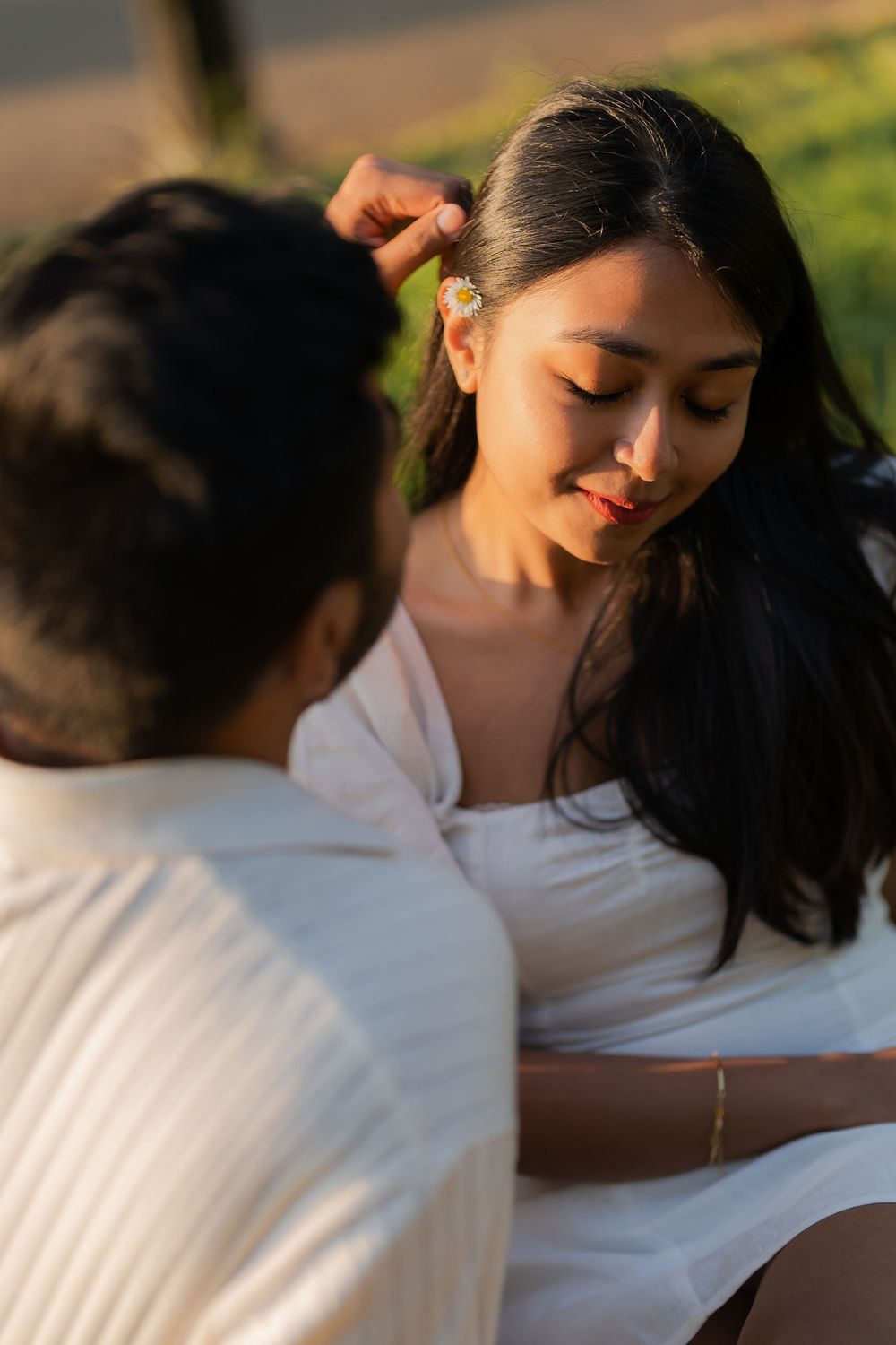 A man gently places a flower in a smiling woman's hair during a romantic golden hour outdoor moment.