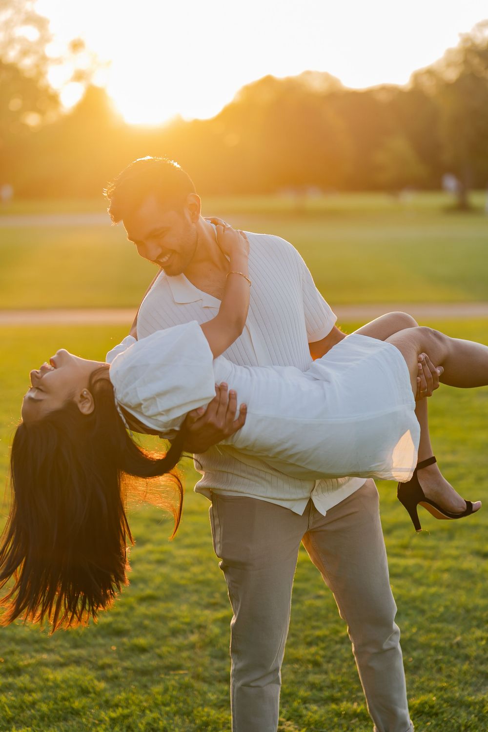 Groom joyfully lifts bride in golden sunset light during romantic outdoor couples photo session.