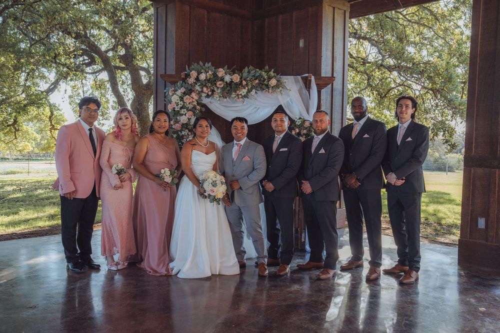Wedding party posing under floral arch at rustic outdoor ceremony venue.