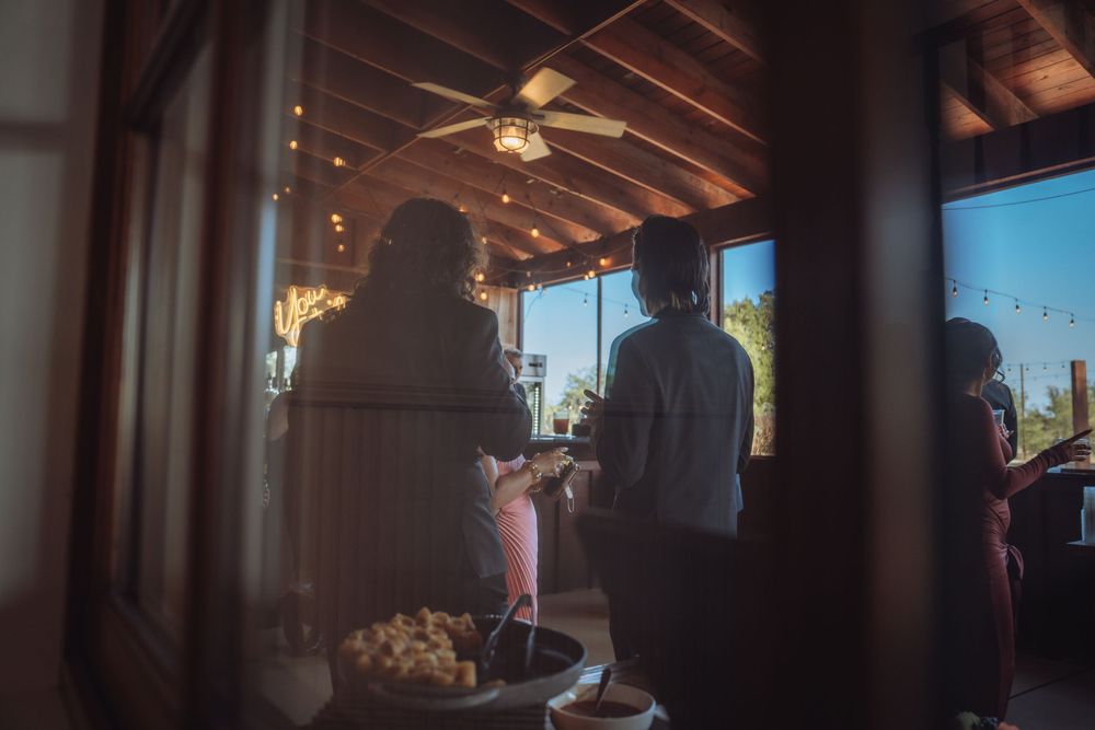 Wedding guests mingling inside warmly lit rustic venue with ceiling fan.