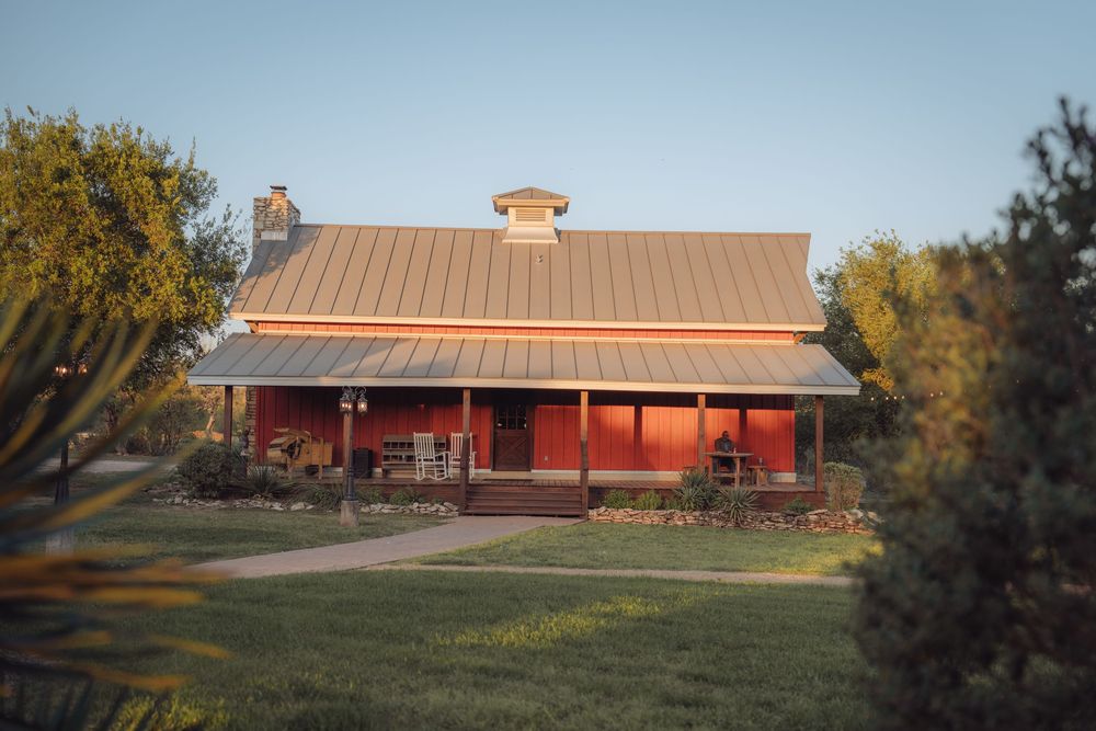 Rustic red farmhouse venue with metal roof surrounded by lush greenery at dusk.