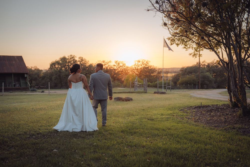 Bride and groom walking hand-in-hand toward stunning golden sunset at outdoor venue.