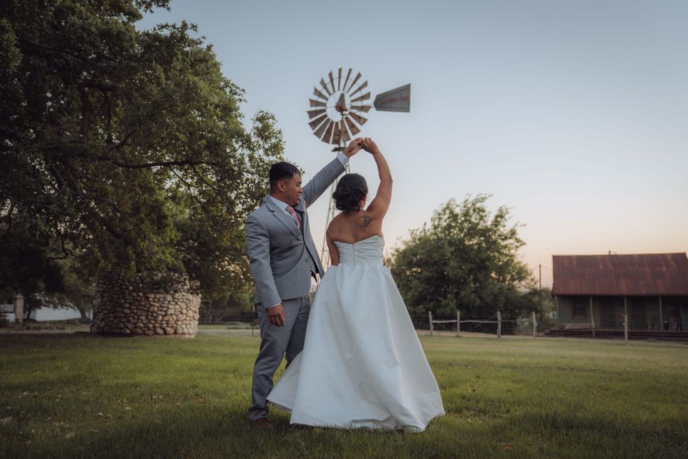 Bride and groom posing playfully by a rustic windmill on a farm at dusk during their outdoor wedding.